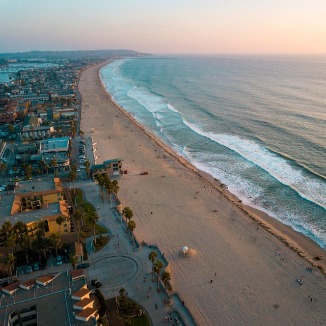 an aerial photo of a beach between the ocean and a city