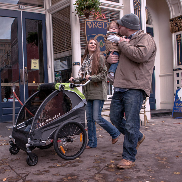 a couple walking down the street pushing a stroller and holding a toddler