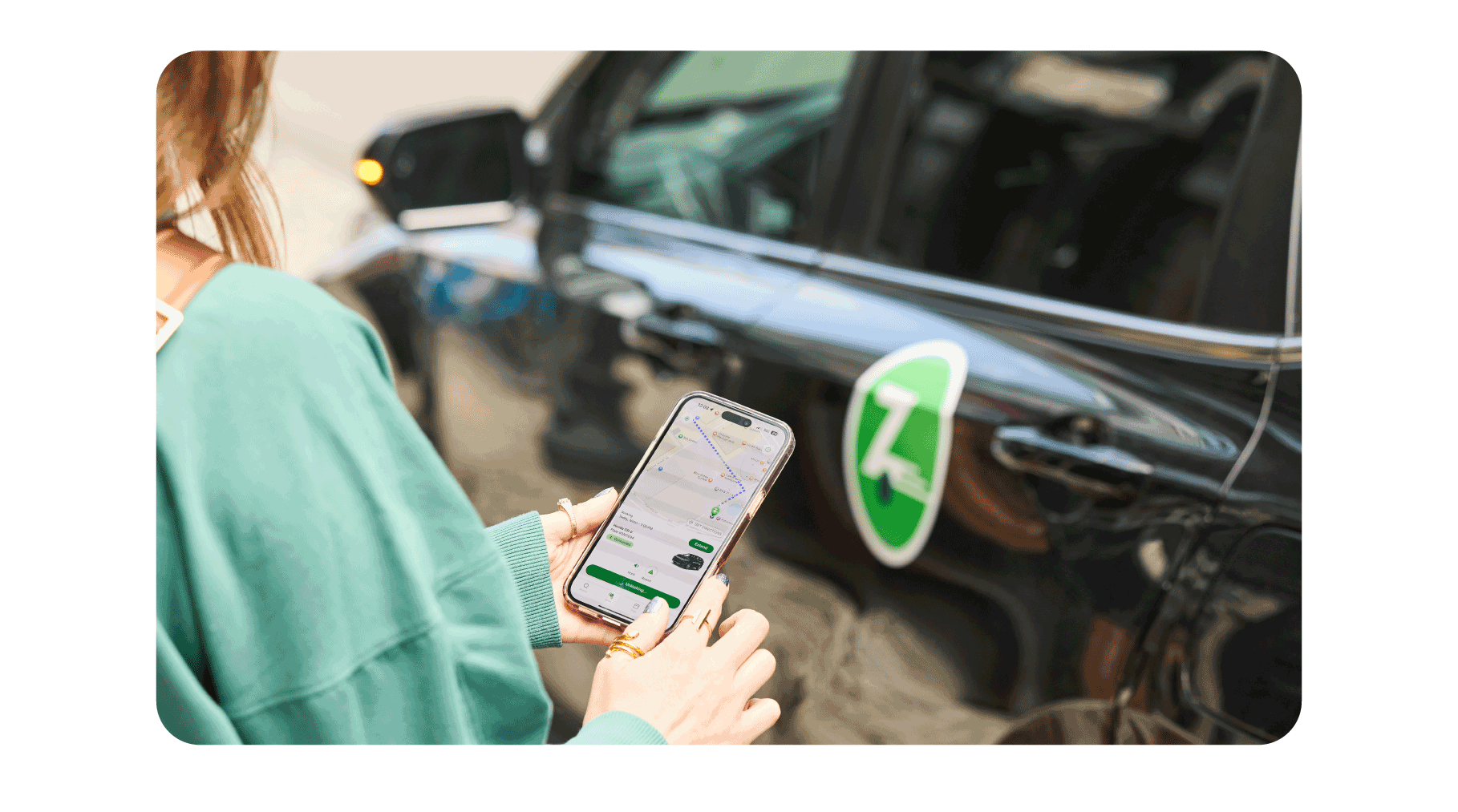 Woman looking at the Zipcar app on her phone standing next to a black zipcar