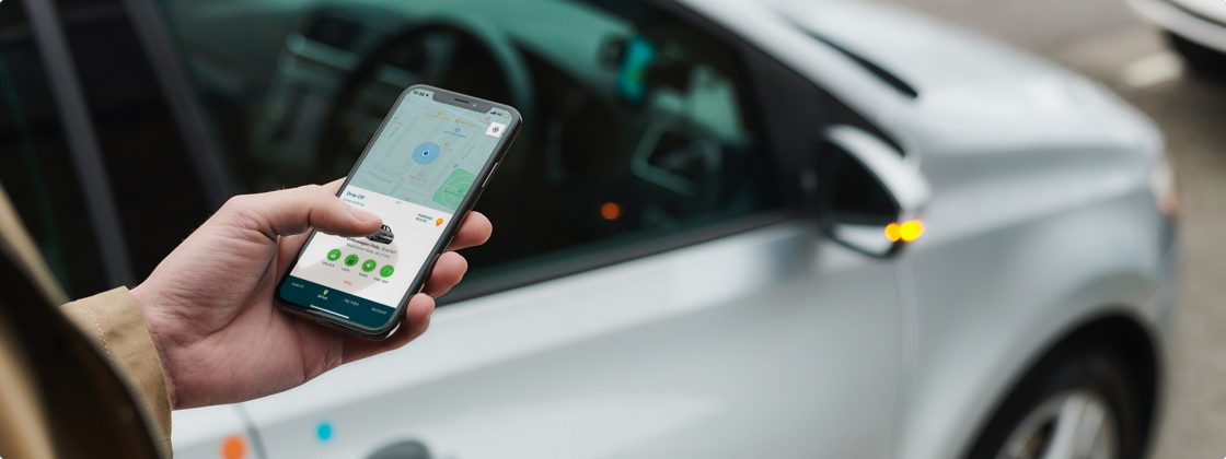 a hand holding a cell phone with a zipcar in the background