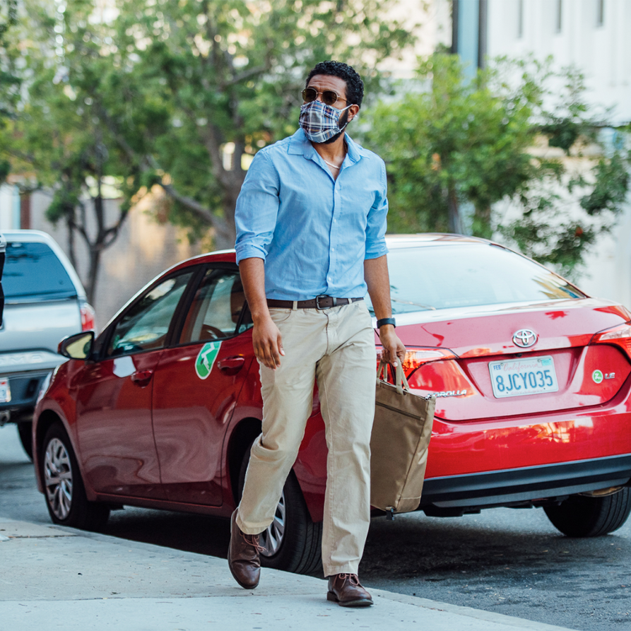 Man wearing blue dress shirt walking past red Toyota Corolla