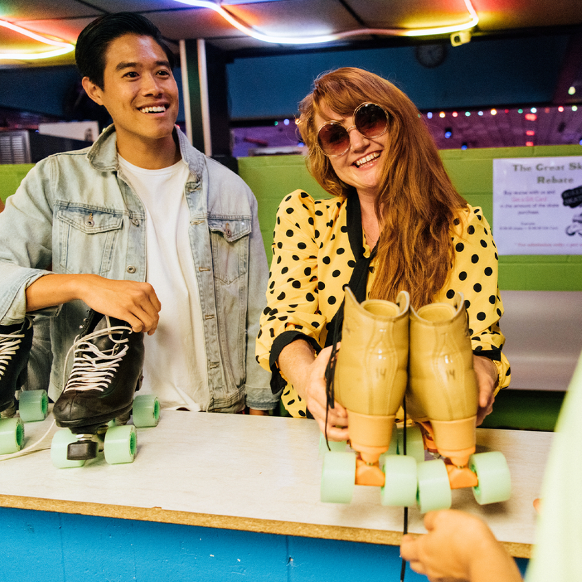 Man in denim jacket and woman in yellow polka dot coat, smiling and holding roller skates. 