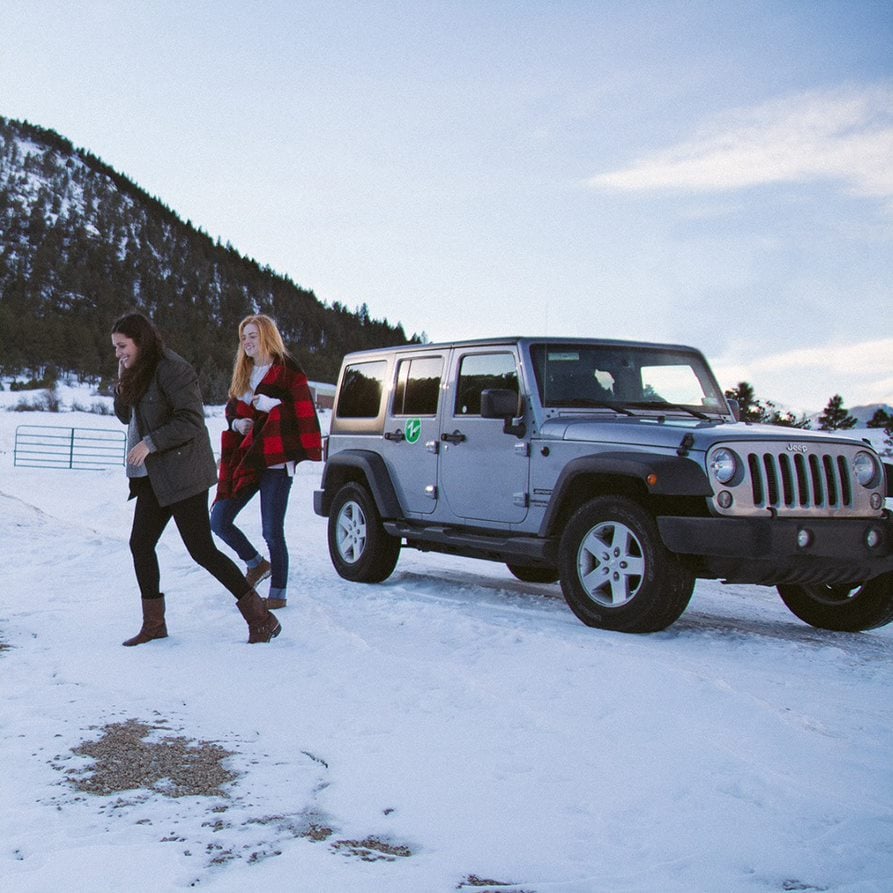 Girls standing in snow by a Jeep Zipcar