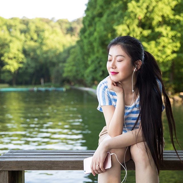 woman sitting next to the water with eyes closed and headphones in