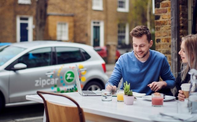 Friends sitting at a table with a Zipcar in the background