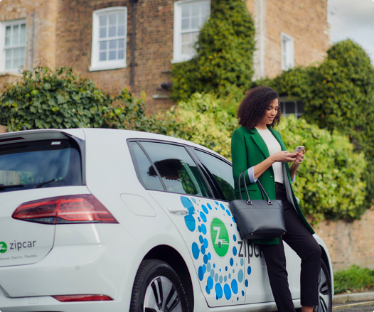 woman leaning against the size of a car while using cell phone